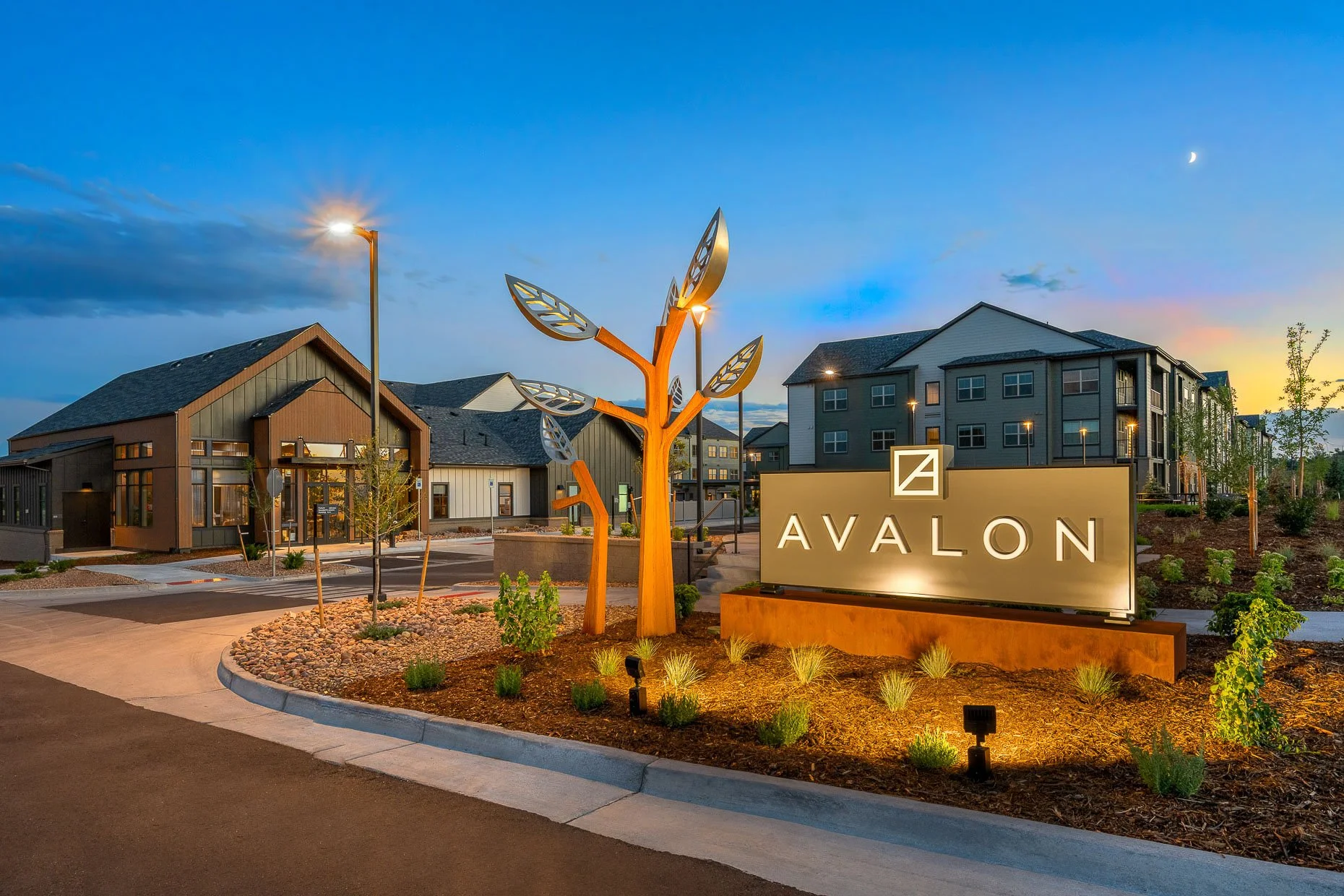 Multi-family front exterior at dusk with creative lighting on monument and professional landscaping.