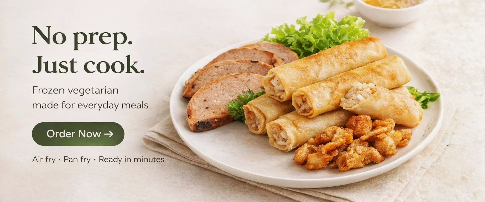 Plate of vegetarian fried spring rolls, slices of vegetarian meatloaf, fried chicken, lettuce, and cilantro on a white plate, with a small bowl of dipping sauce in the background.