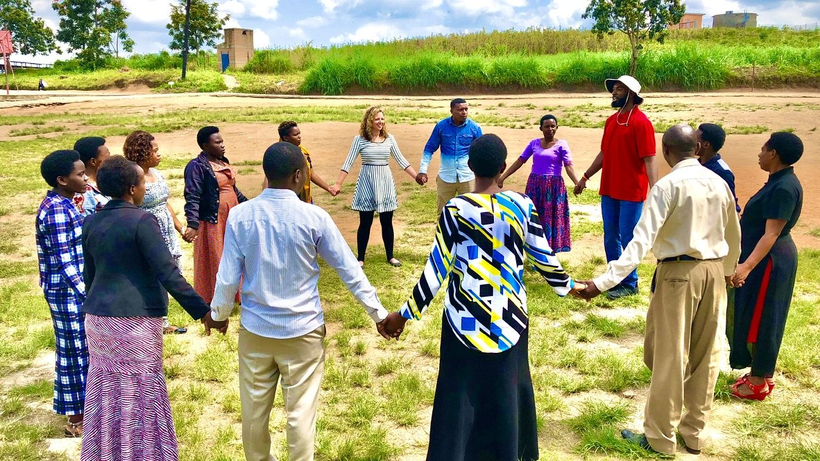 A diverse group of people holding hands in a circle outdoors on a grassy field.