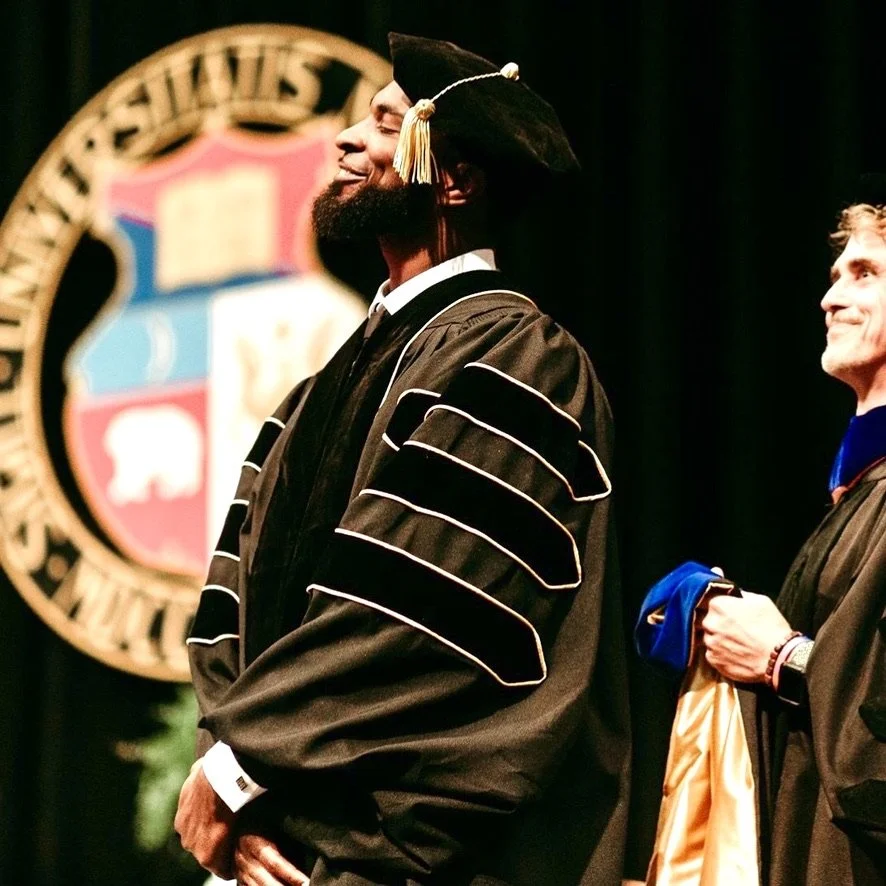 Graduate in cap and gown smiling during a ceremony on stage.