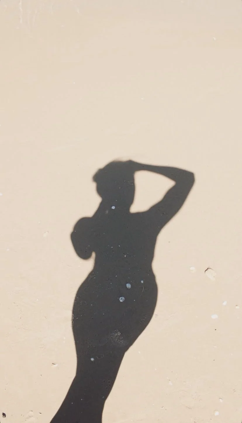 Shadow of a woman posing with one arm behind her head on a plain background.