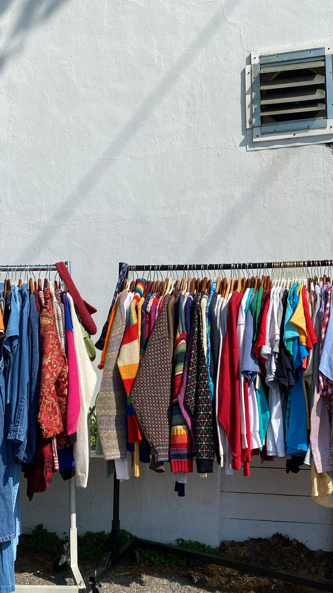 Clothes hanging on racks outdoors against a white wall with an air vent.