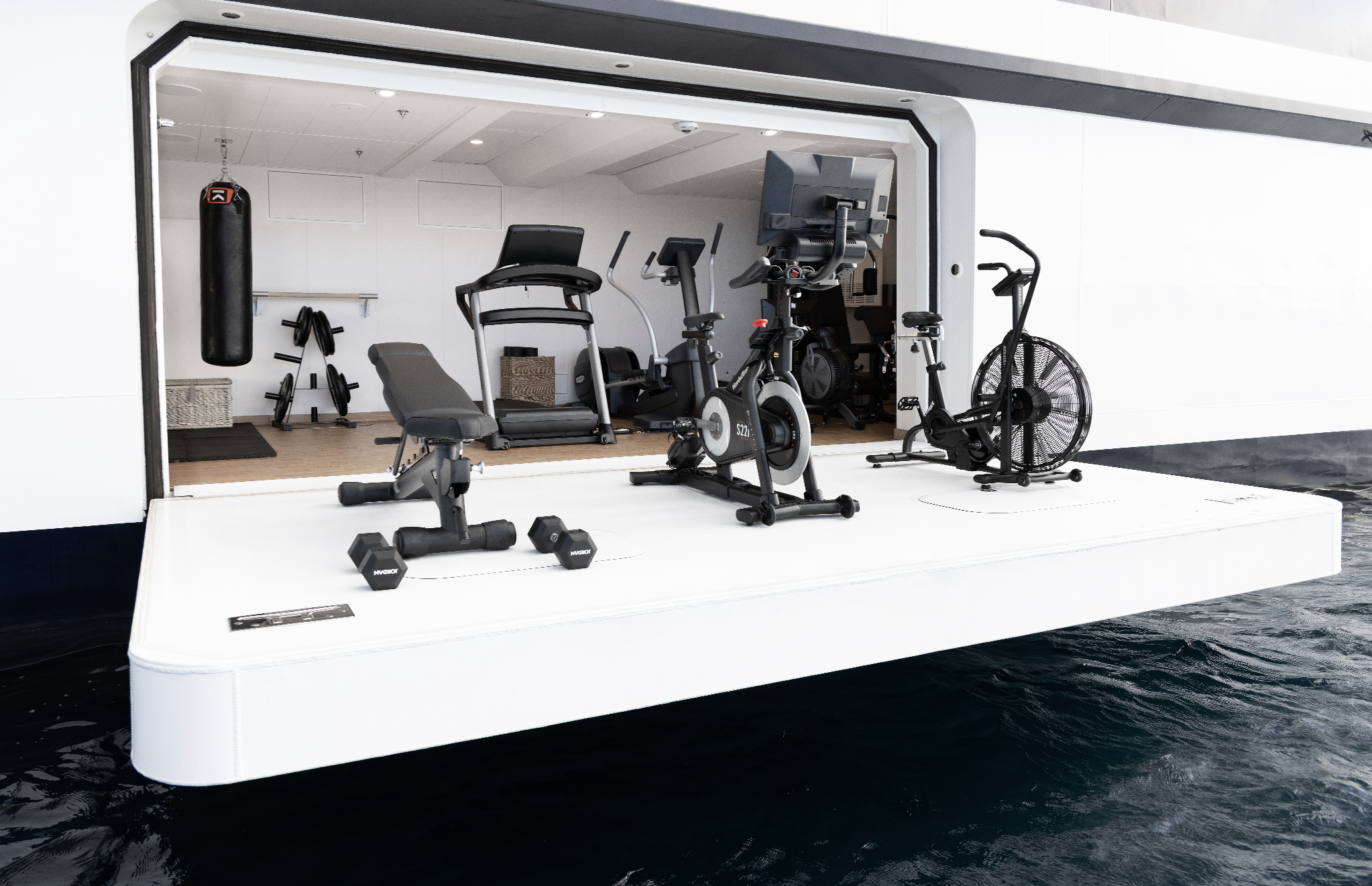 Fitness equipment including a treadmill, exercise bike, elliptical trainer, dumbbells, and a punching bag inside a floating gym on water.