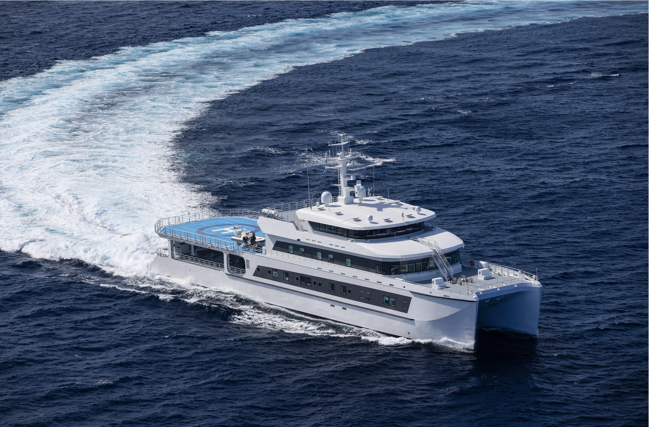 Large white motor yacht with a helipad on the back, cruising on the ocean, leaving a trail of wake behind.