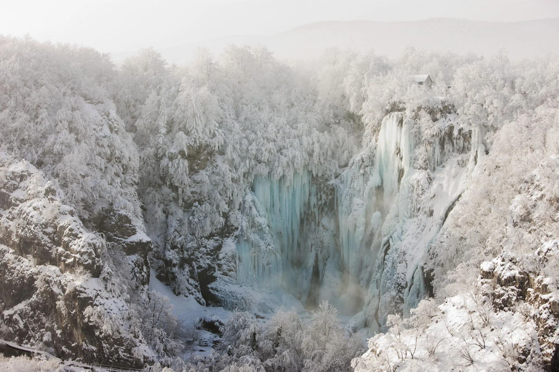 Plitvice lakes, Plitvicka jezera, Croatia, Hrvatska, Snow-covered trees and cliffs surrounding a frozen waterfall in a winter landscape.