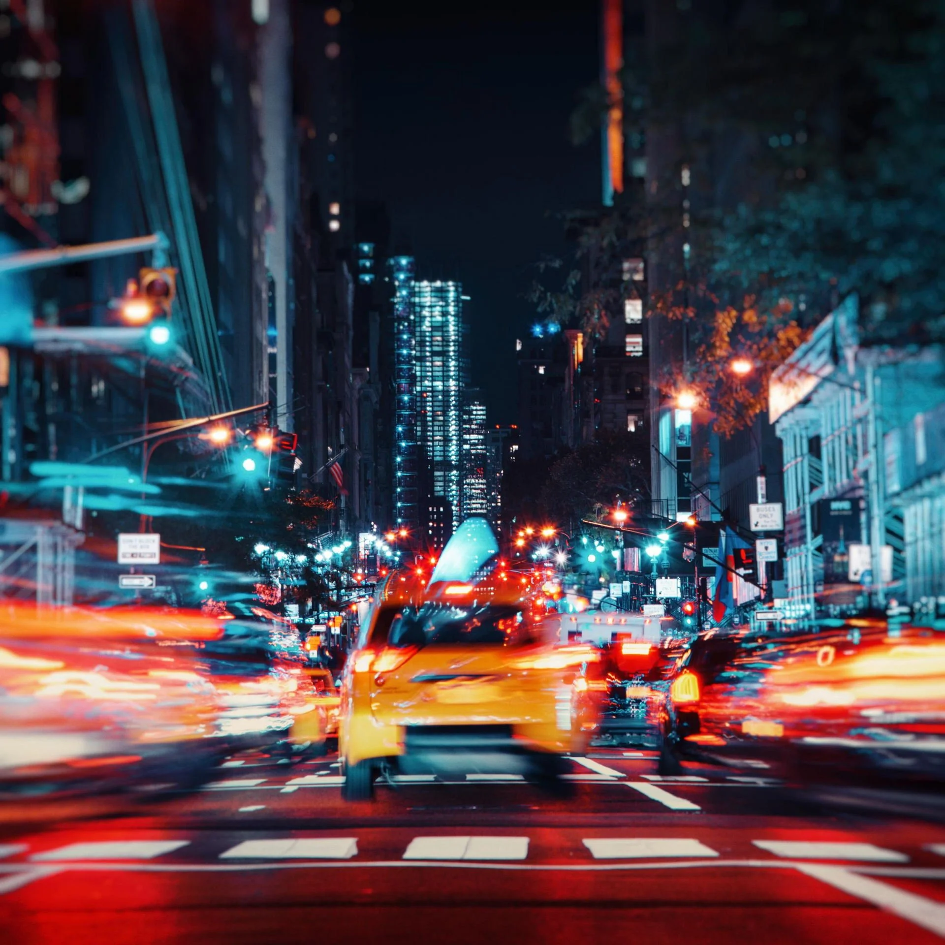Night city street illuminated with colorful lights, blurred moving cars, and tall buildings in the background.