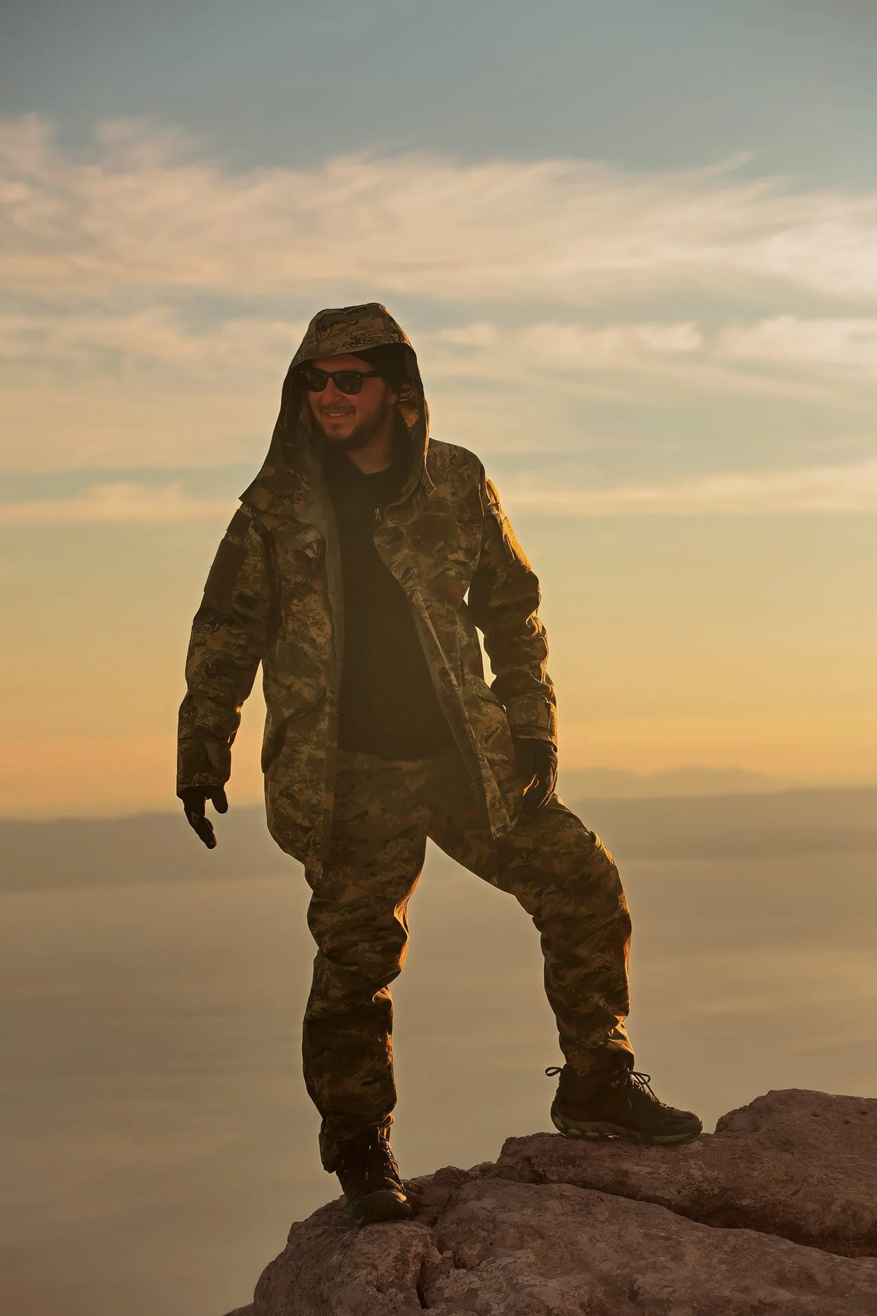 Dražen Stojčić, photographer from Osijek, Croatia. A man in camouflage clothing and sunglasses standing on a rocky ledge during sunset.
