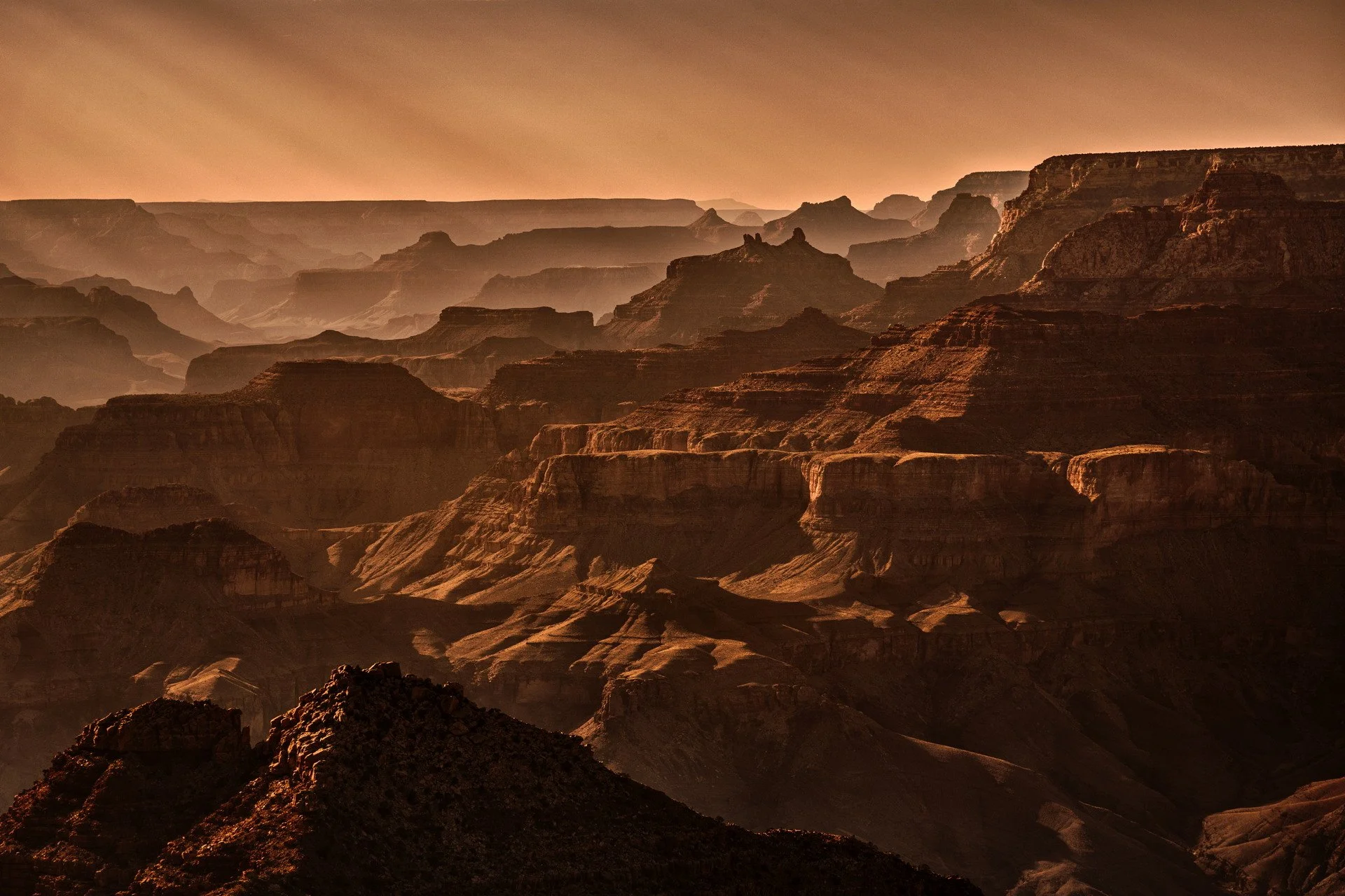 Sunset over the Grand Canyon, with layered rock formations and a warm orange sky.