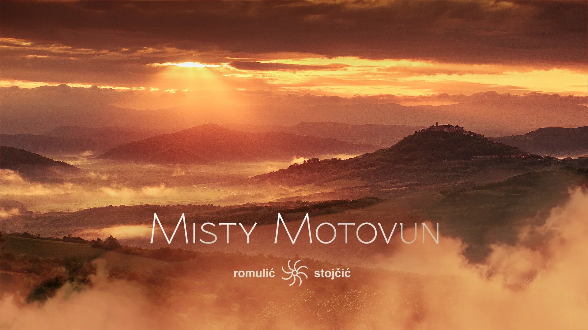 A scenic landscape of rolling hills at sunrise with mist and clouds in the sky. The image has the text 'Misty Motovun' and the names 'romulić' and 'stojčić' displayed on it.