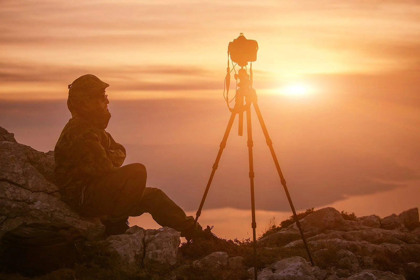Dražen Stojčić, photographer from Osijek, Croatia. Person sitting on rocky terrain during sunset, taking a photograph with a camera mounted on a tripod.