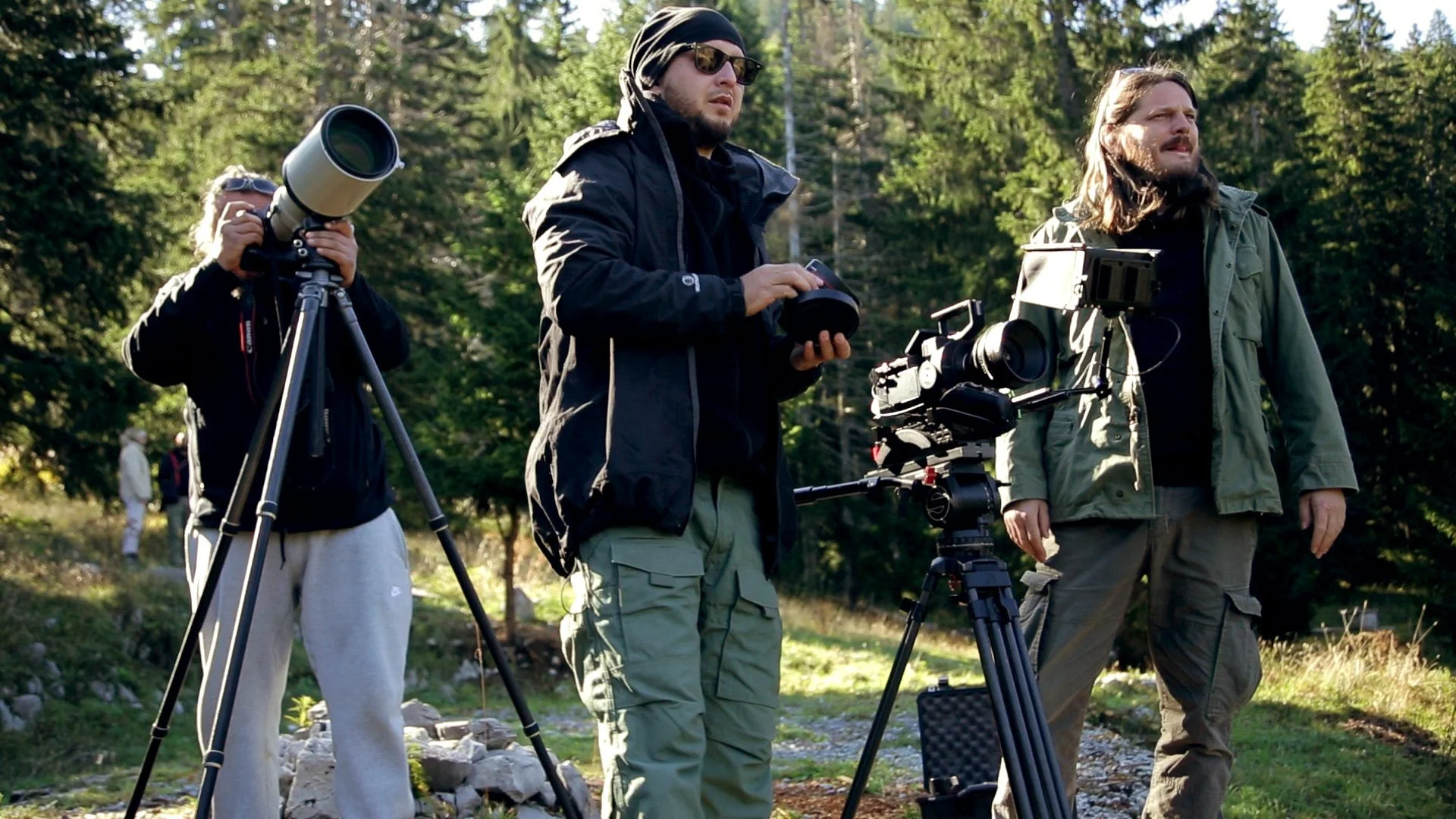 Three men filming a scene outdoors in a forested area with equipment.