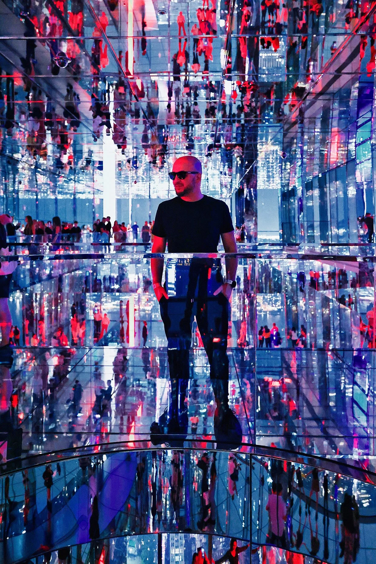 Dražen Stojčić, photographer from Osijek, A person with sunglasses and a black shirt standing in a mirrored, colorful light installation with reflections of visitors.