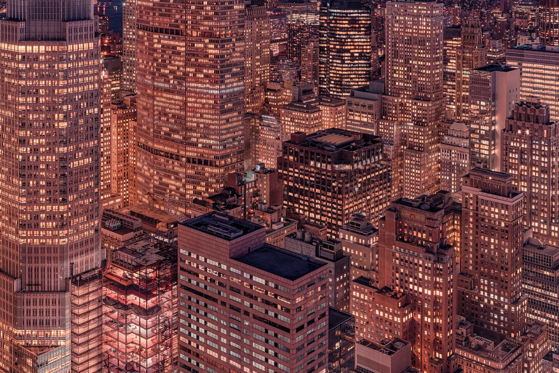 Nighttime cityscape of tall, illuminated skyscrapers densely packed in Manhattan, New York City.