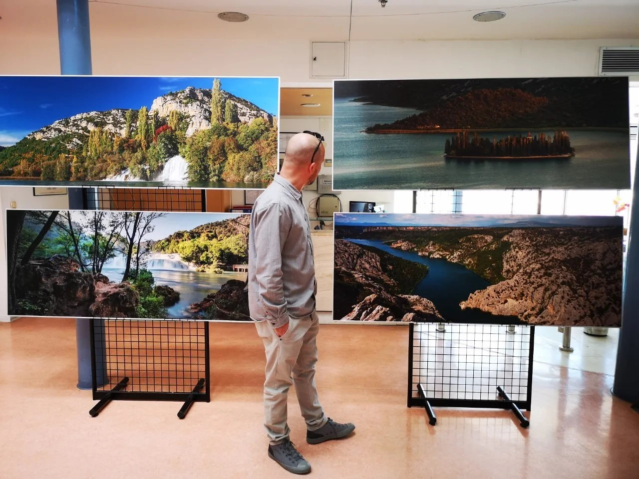 A man stands in front of outdoor landscape photographs on display panels, looking at the images of rivers, waterfalls, islands, and mountains.