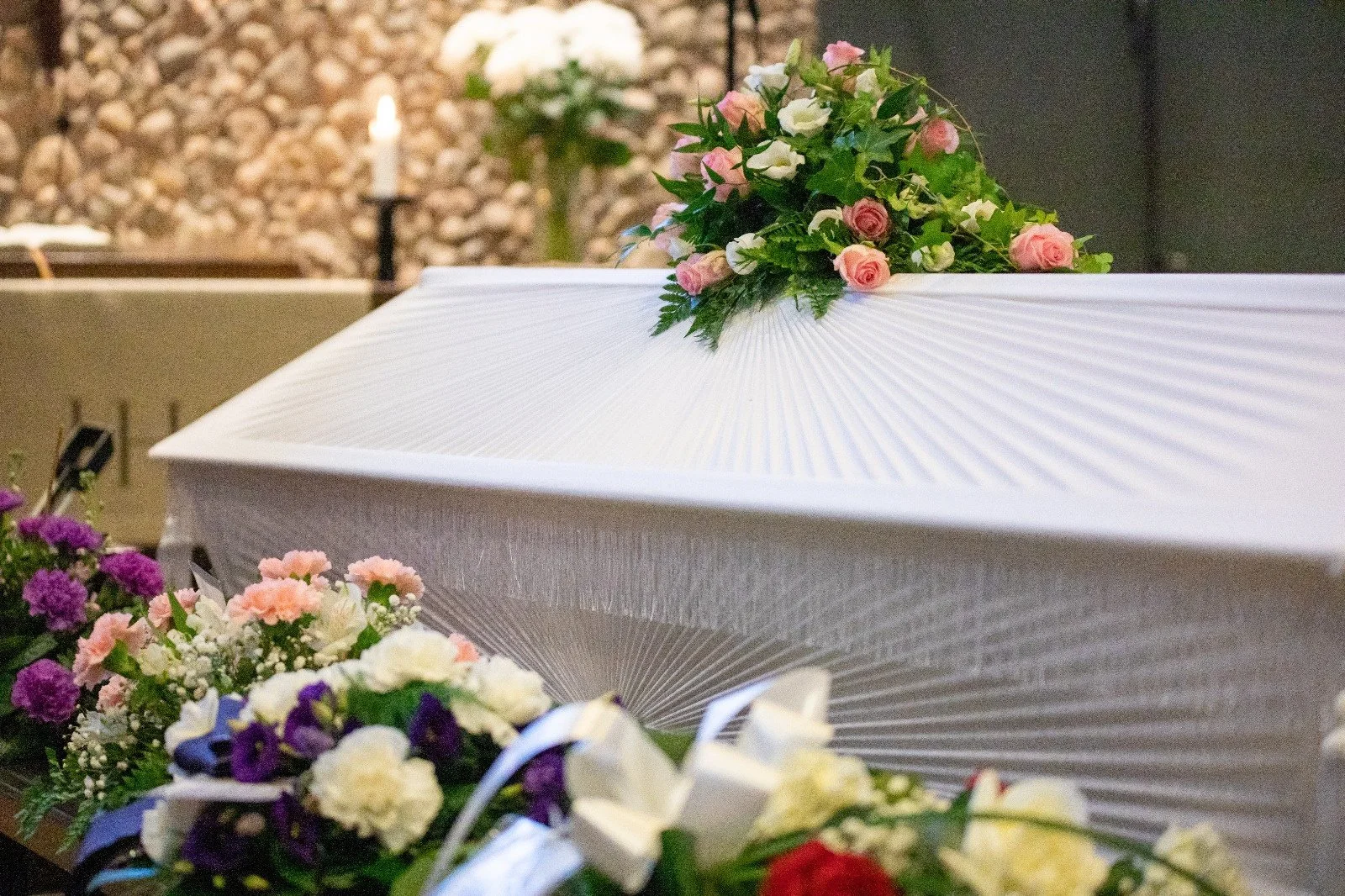 Kuvassa valkoinen arkku kirkossa kukkien ympäröimänä.