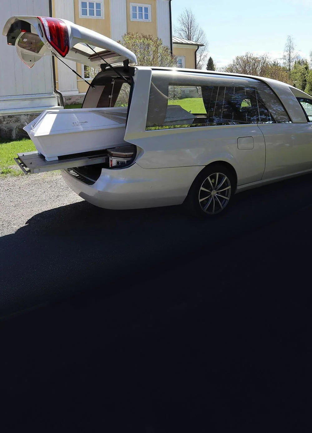 Da-Pu hautauspalvelun vaalea auto kirkon edessä, osittain auton sisällä valkoinen arkku.