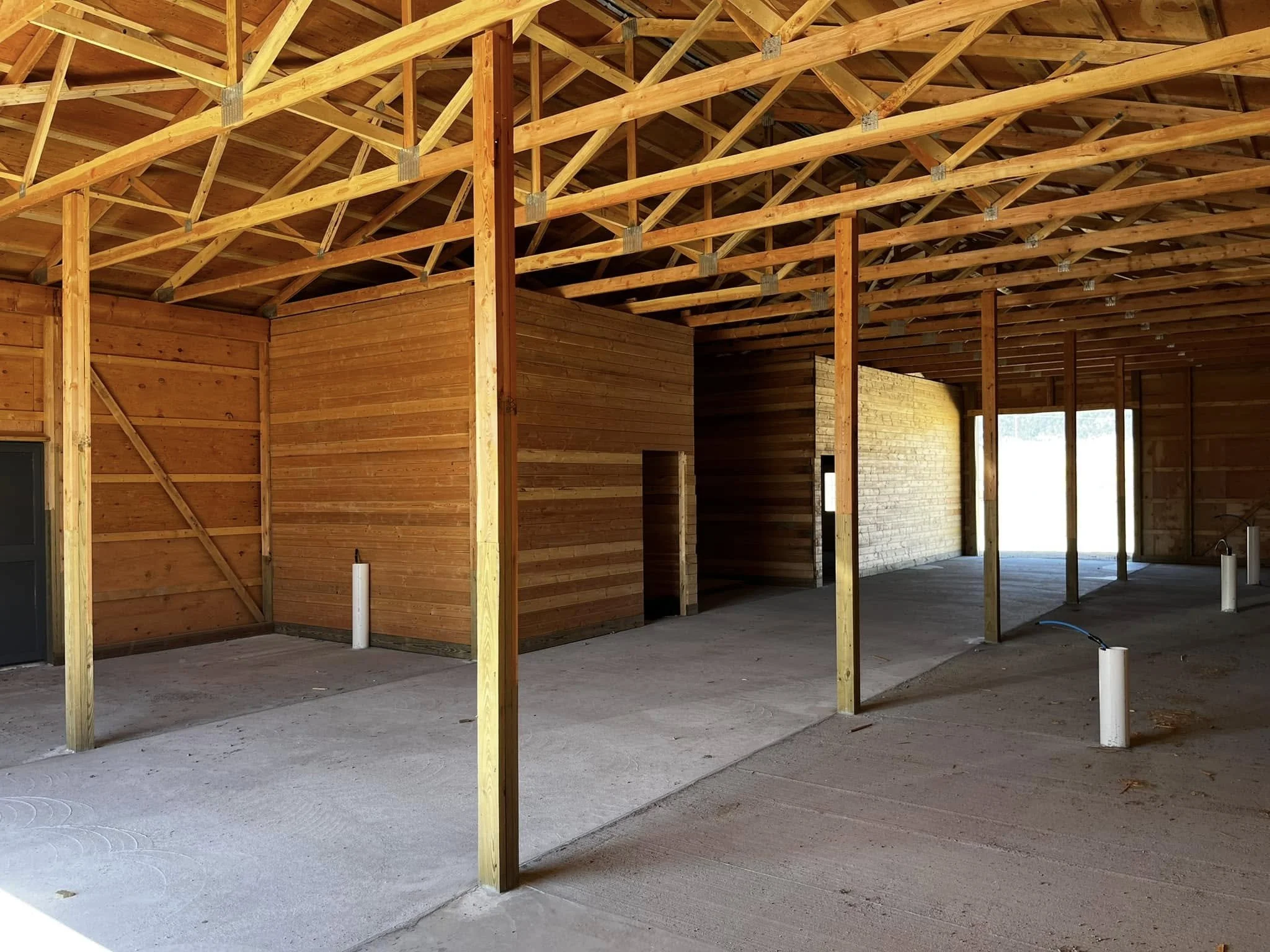 Interior of a building under construction with wooden framing, walls, and roof, and exposed concrete floor.