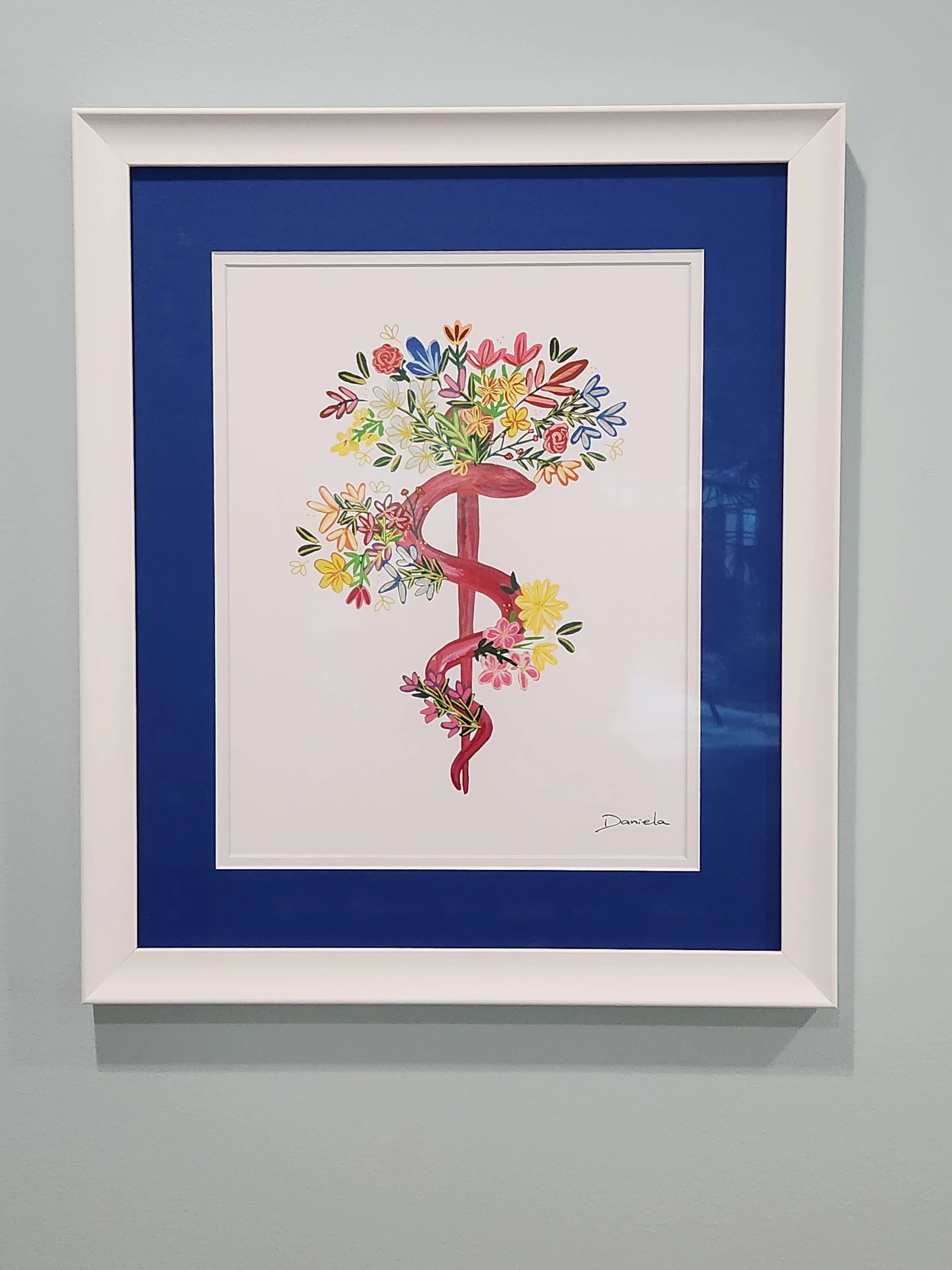 A framed artwork featuring a pink caduceus symbol entwined with a snake, with a large bouquet of colorful flowers growing from the top.