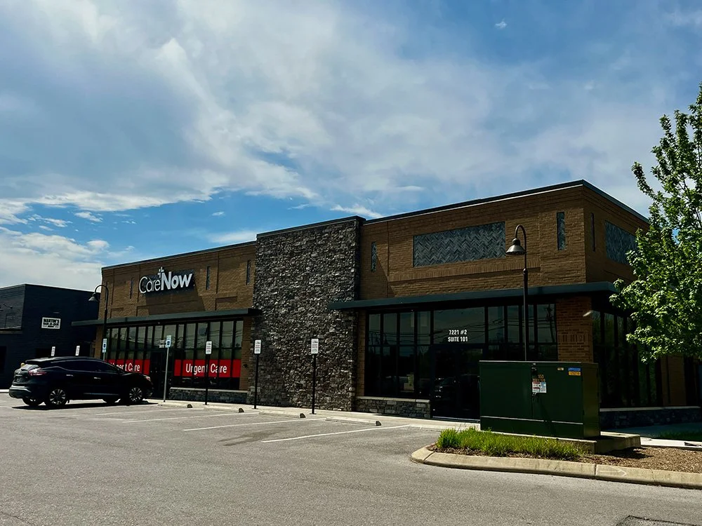 Exterior view of a medical clinic building named 'CareNow' with a parking lot in front, some cars, and clear weather.