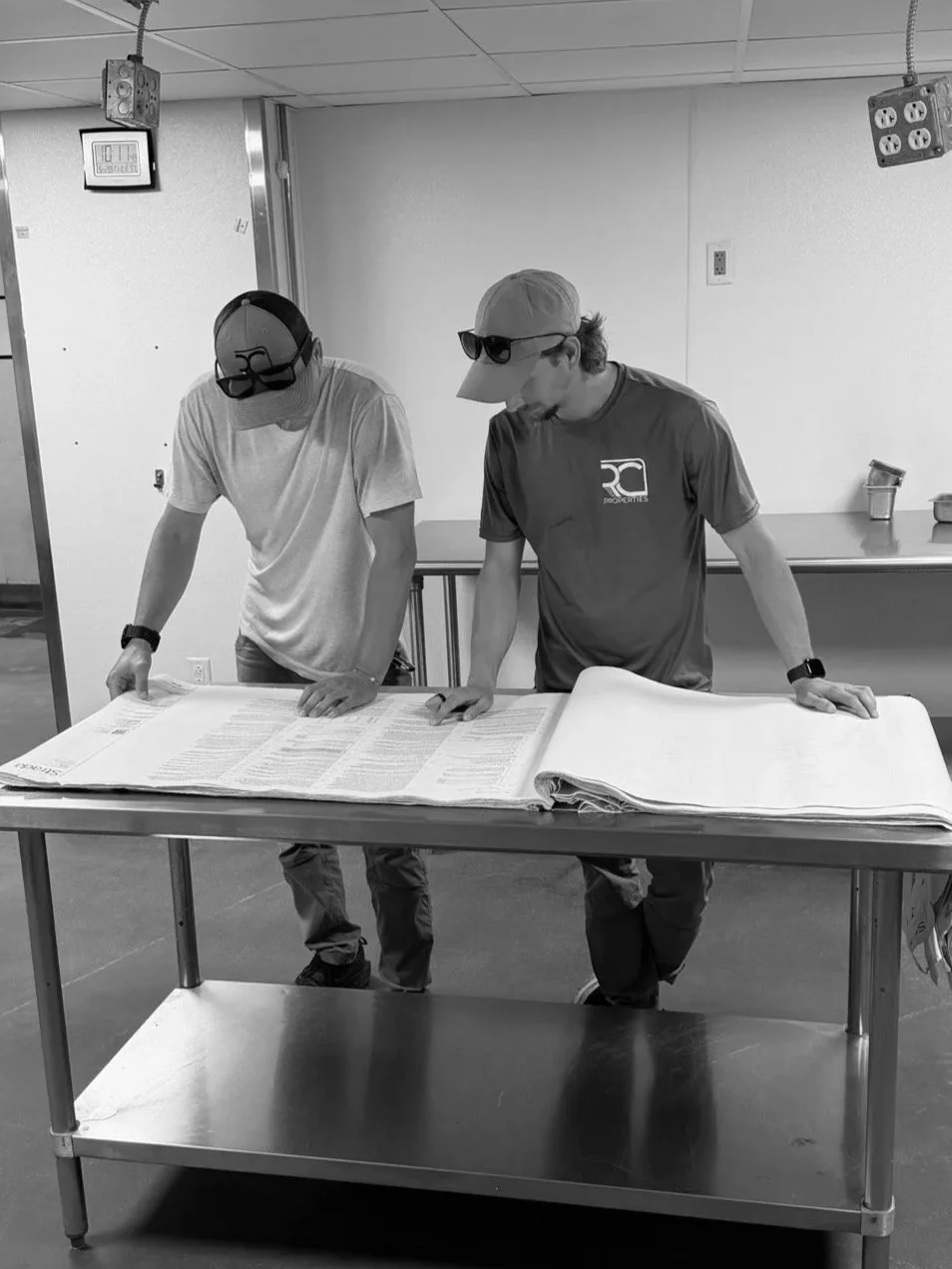 Two men looking at large documents on a table in an industrial or warehouse setting.