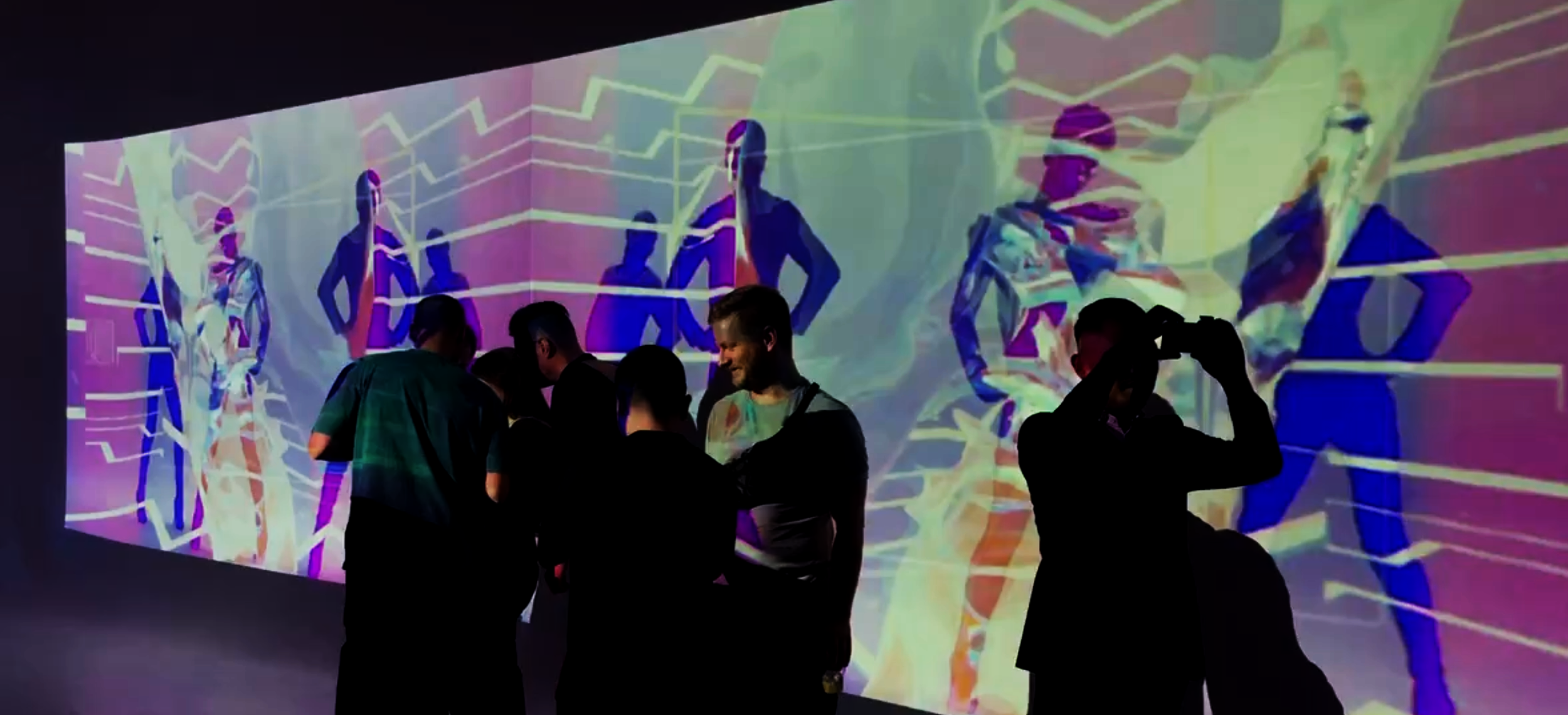People standing in front of a large, colorful digital art installation with abstract human figures and geometric shapes projected onto the wall.