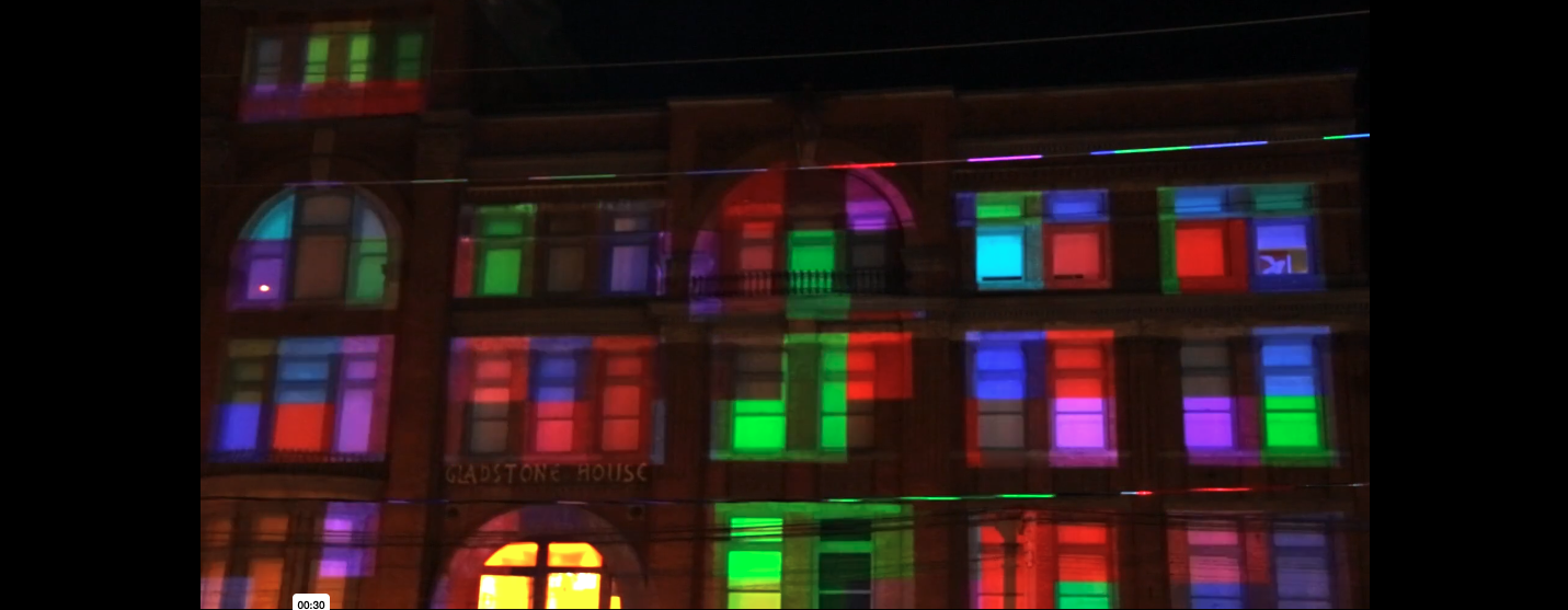 Building with colorful light projections resembling digital pixels, with the sign 'Gladstone House' on the front.