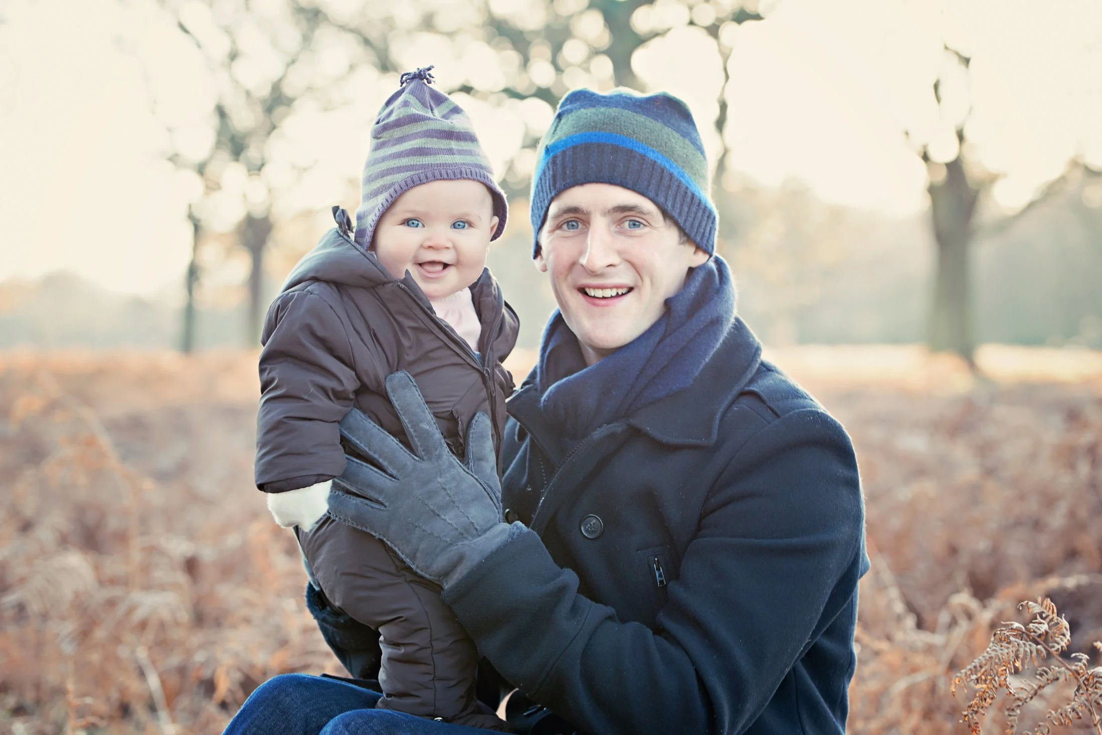 Beautiful fine art family photoshoot of a smiling man holding a smiling baby girl outdoors in Richmond Park in the autumn.