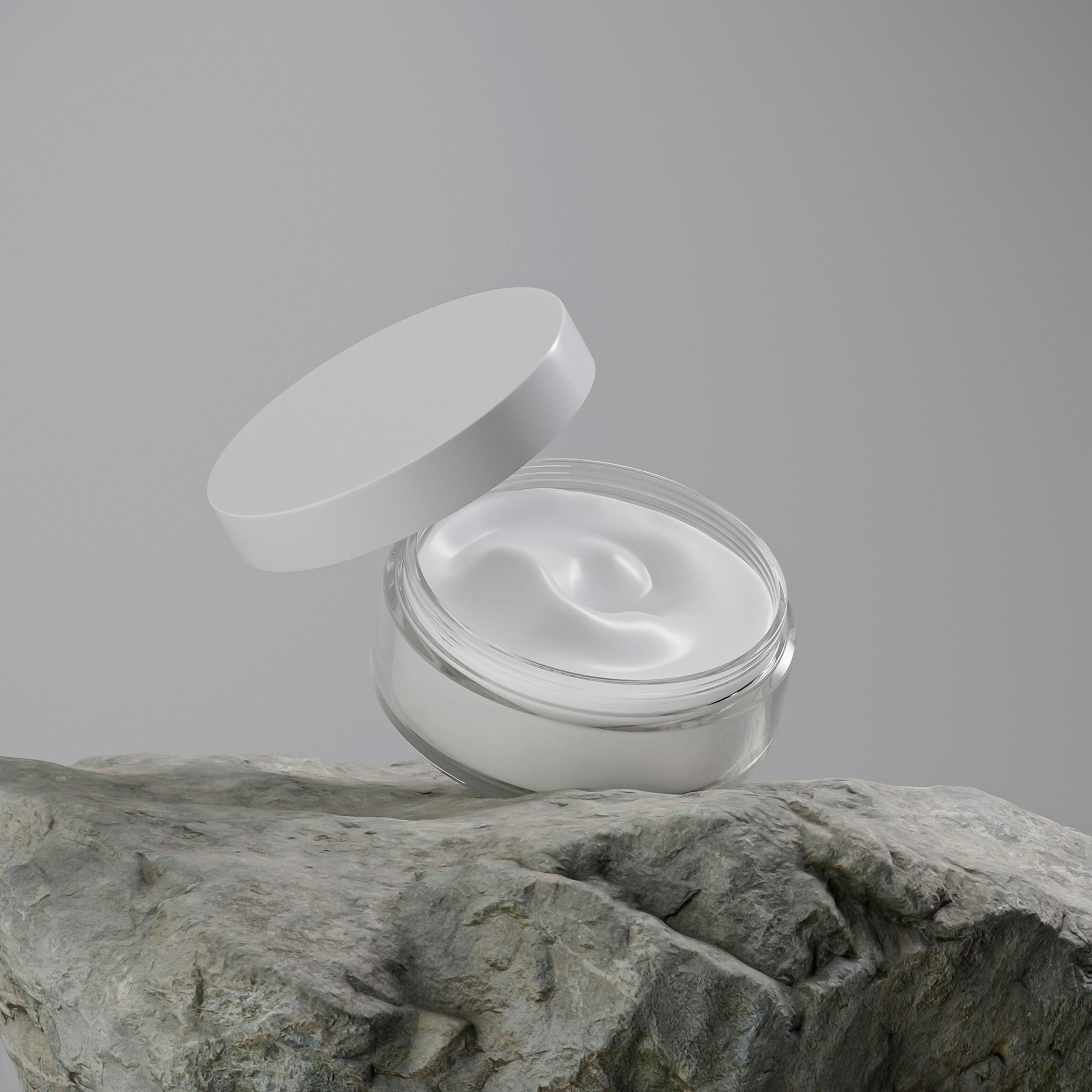 Open jar of white cream or moisturizer on a rocky surface.