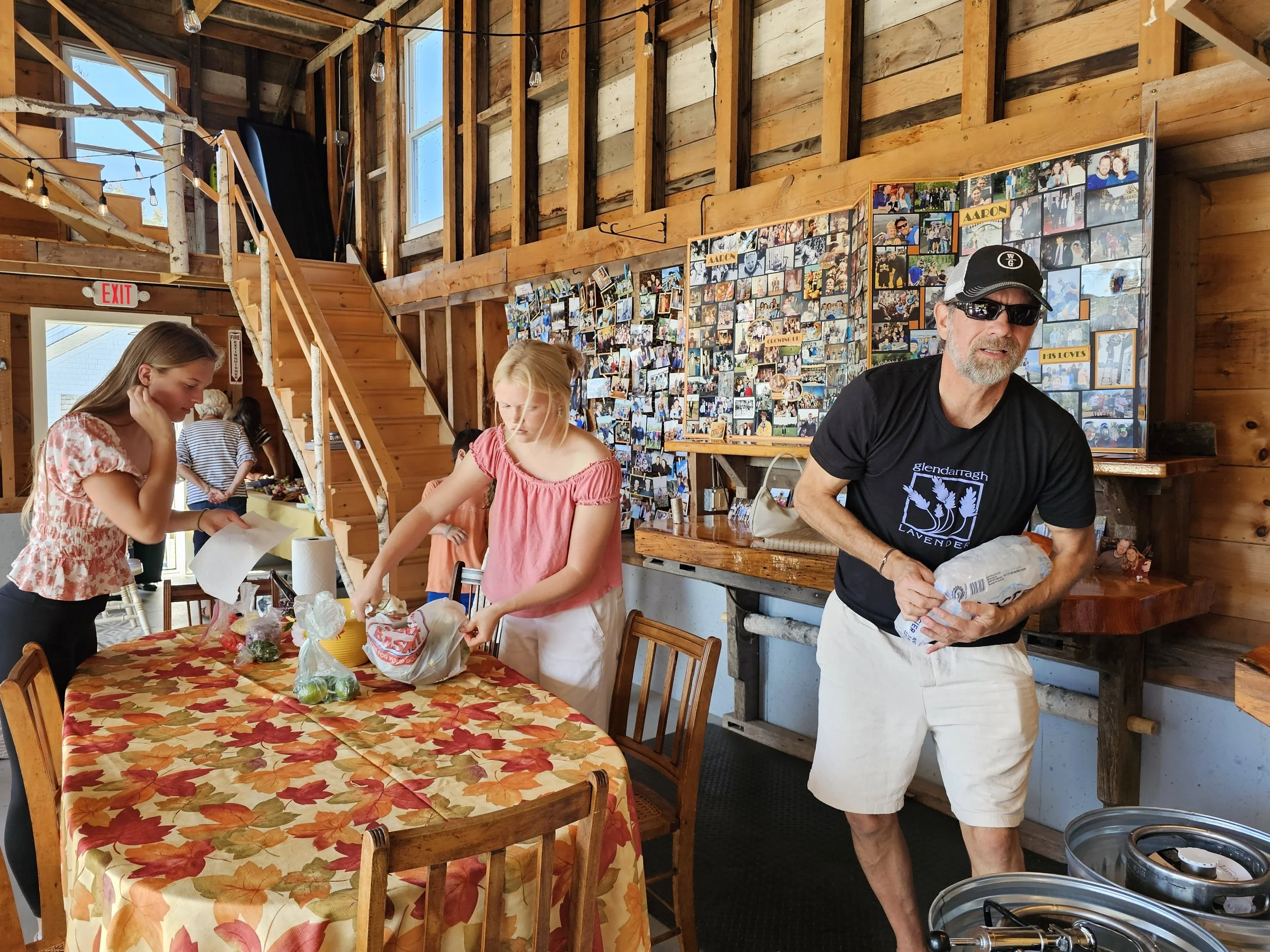 People preparing food at a gathering inside a wooden cabin with photos on display on the wall.