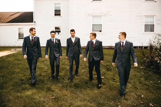 Five men in suits walking across a grassy yard in front of a white house.