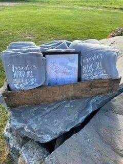 A wooden tray with rolled blue blankets and a framed photo, set on a flat rock outdoors with green grass in the background.