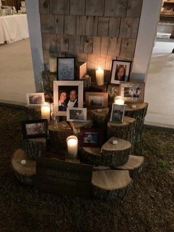A memorial display arranged on large tree stump slices with framed photographs and lit candles.