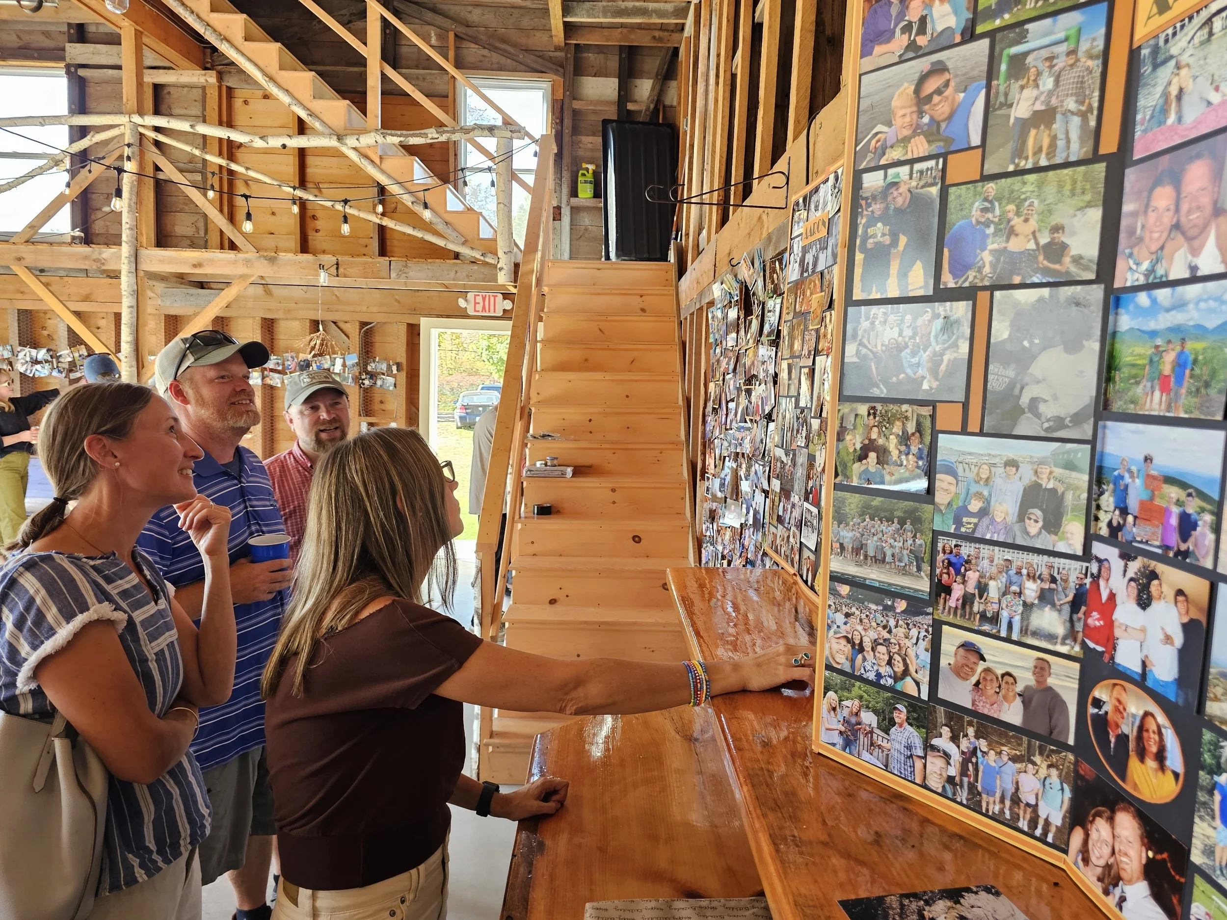People looking at a display board with numerous photographs in a wooden, rustic indoor setting.