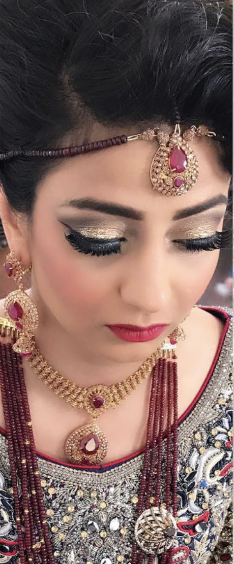 Close-up of a woman wearing elaborate traditional jewelry and makeup, with gold and red jewelry including earrings, necklace, and headpiece, and detailed embroidery on her clothing.
