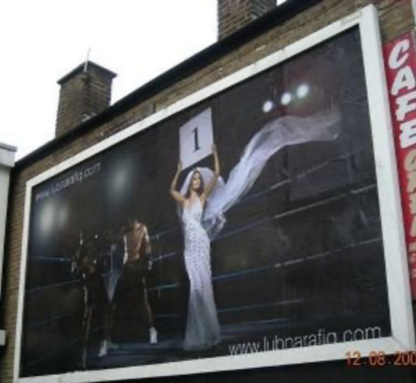A large billboard featuring a woman in a white dress holding a sign with the number 1, standing between two shirtless men, under bright lights.