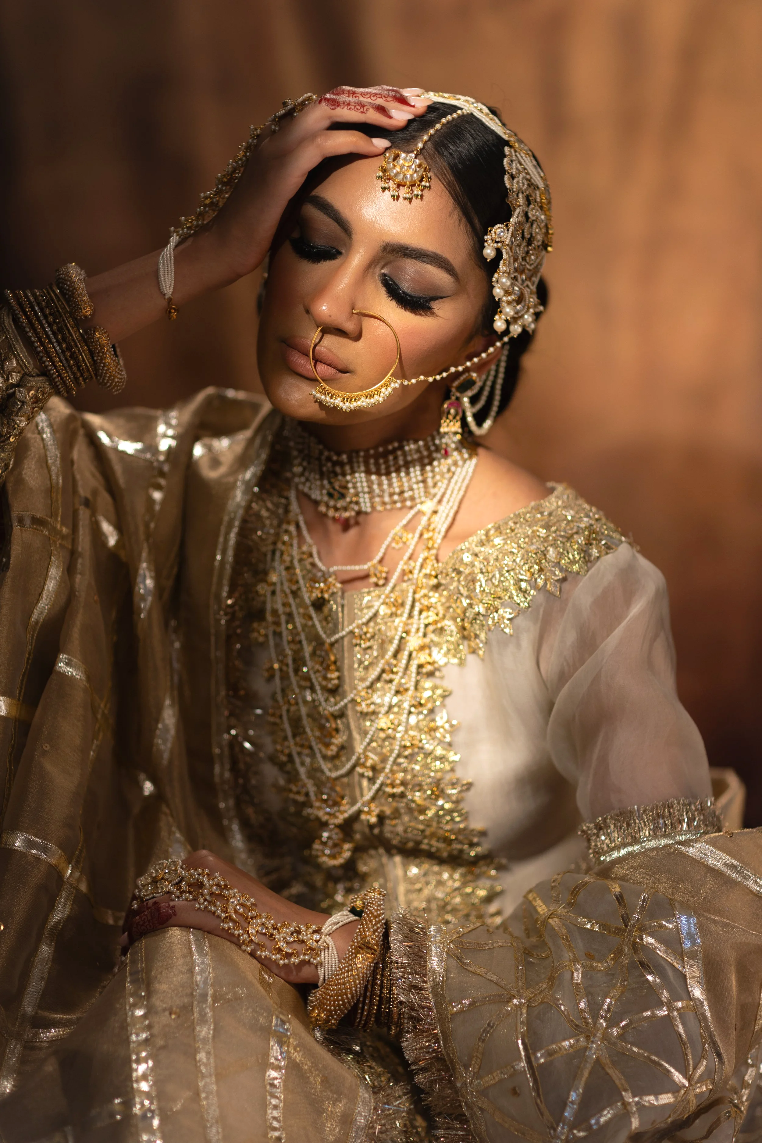 A woman dressed in traditional Indian attire and jewelry, with her eyes closed and one hand resting on her forehead.