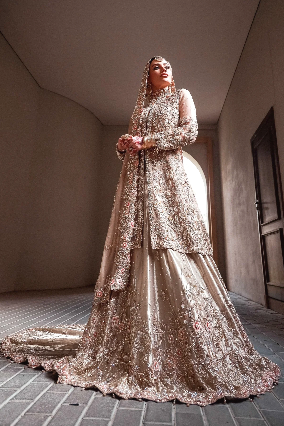 A woman in an ornate, traditional groom's wedding attire, standing indoors with a focused expression.