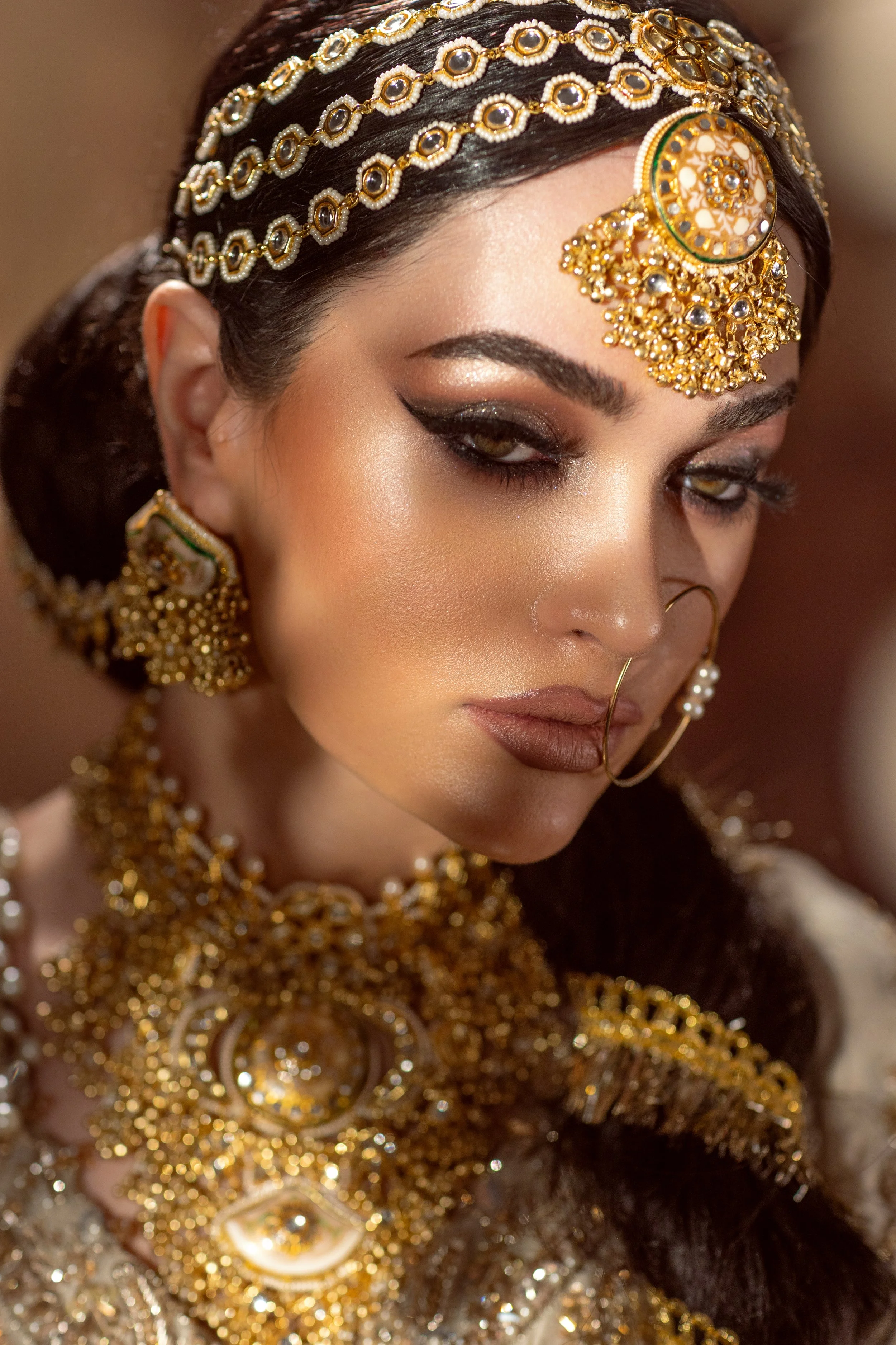 A woman dressed in traditional Indian bridal attire, adorned with elaborate gold jewelry and intricate makeup.