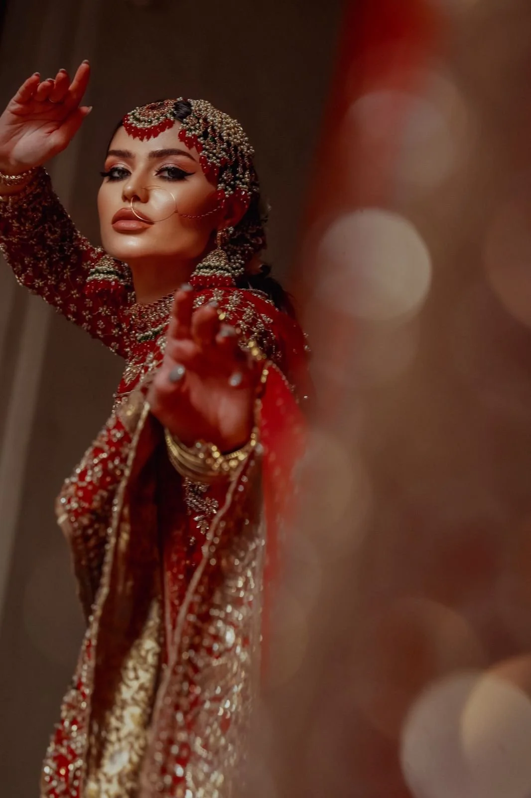 A woman dressed in traditional Indian bridal attire with intricate gold and red jewelry, moving her hands gracefully in a dance pose.