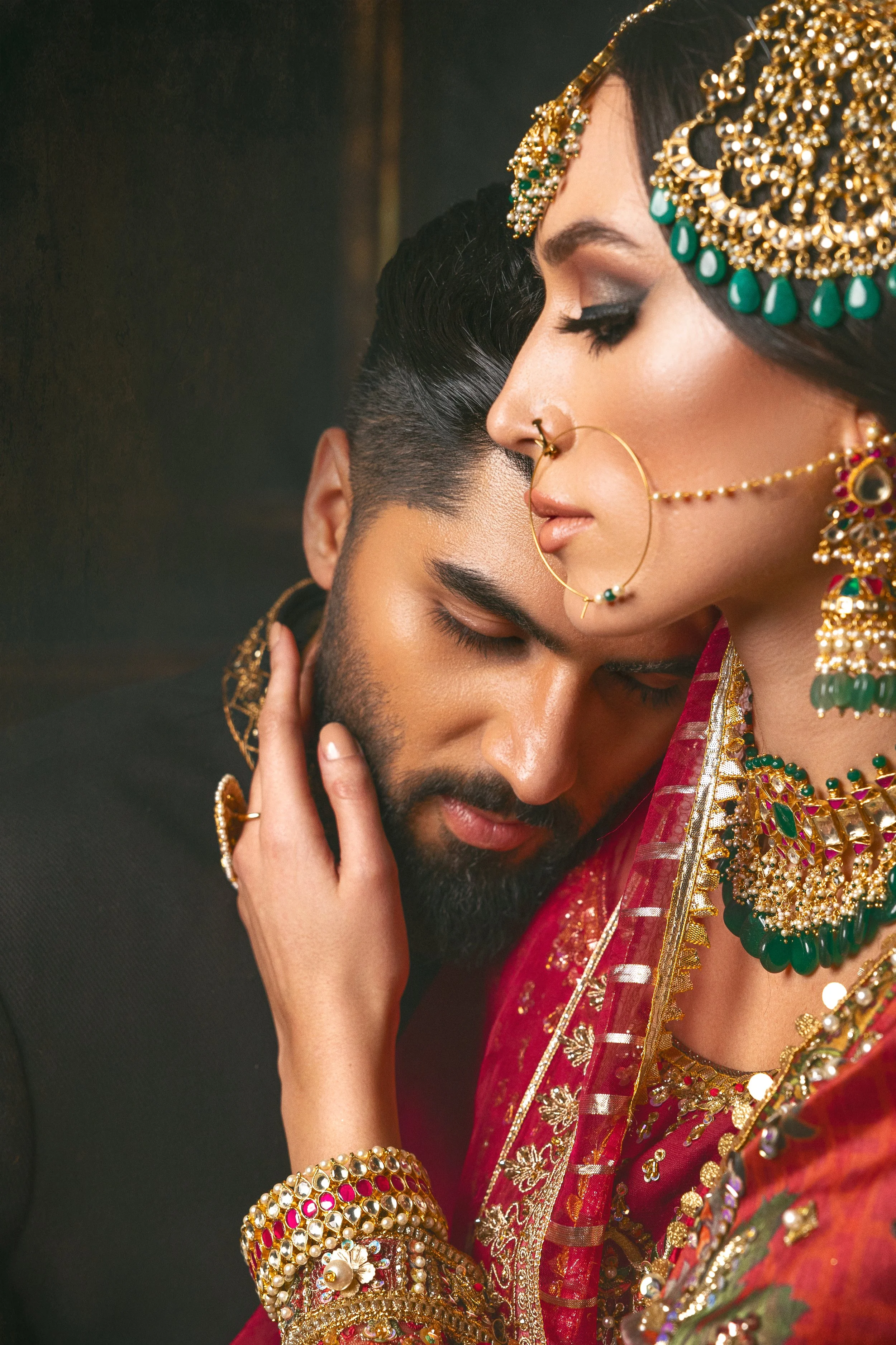 A close-up of a couple with their foreheads touching, dressed in traditional Indian attire and adorned with jewelry, in an intimate pose.