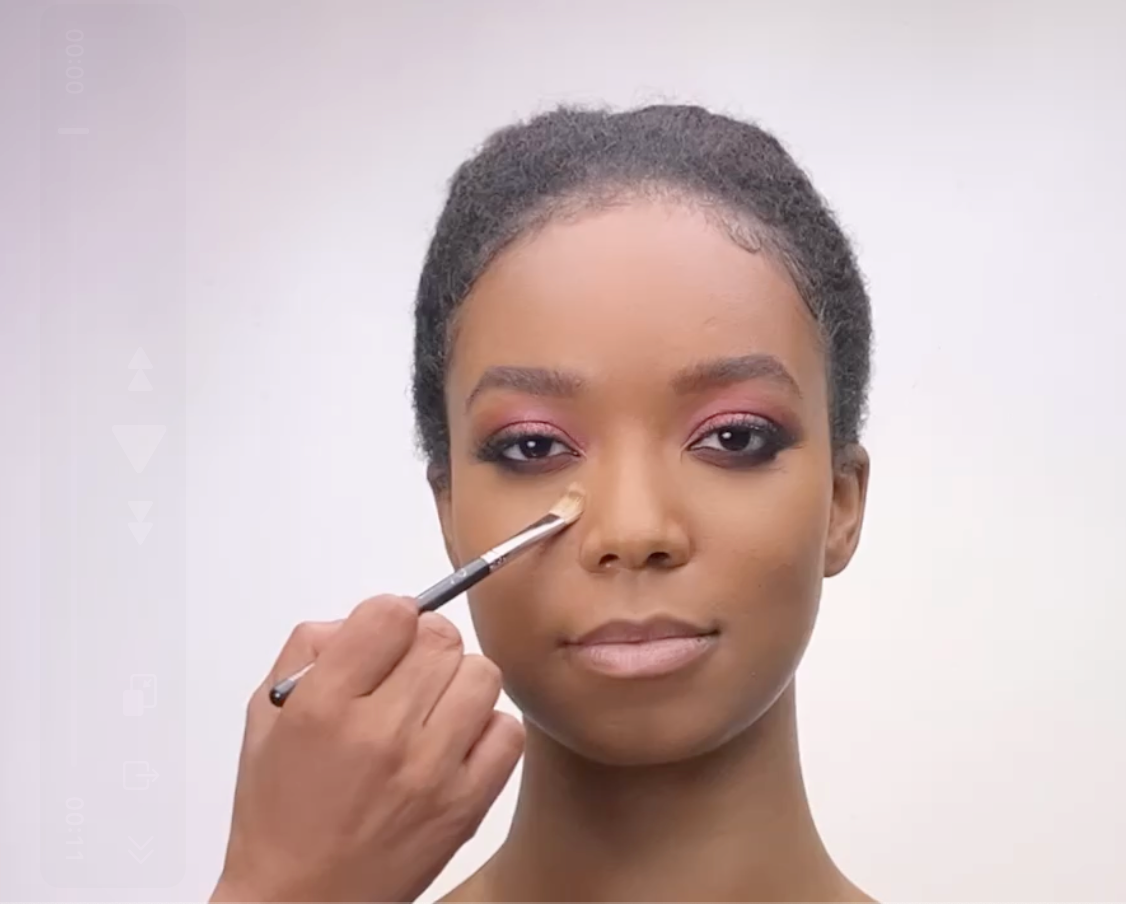 Woman with natural hair having makeup applied under her eye with a brush.