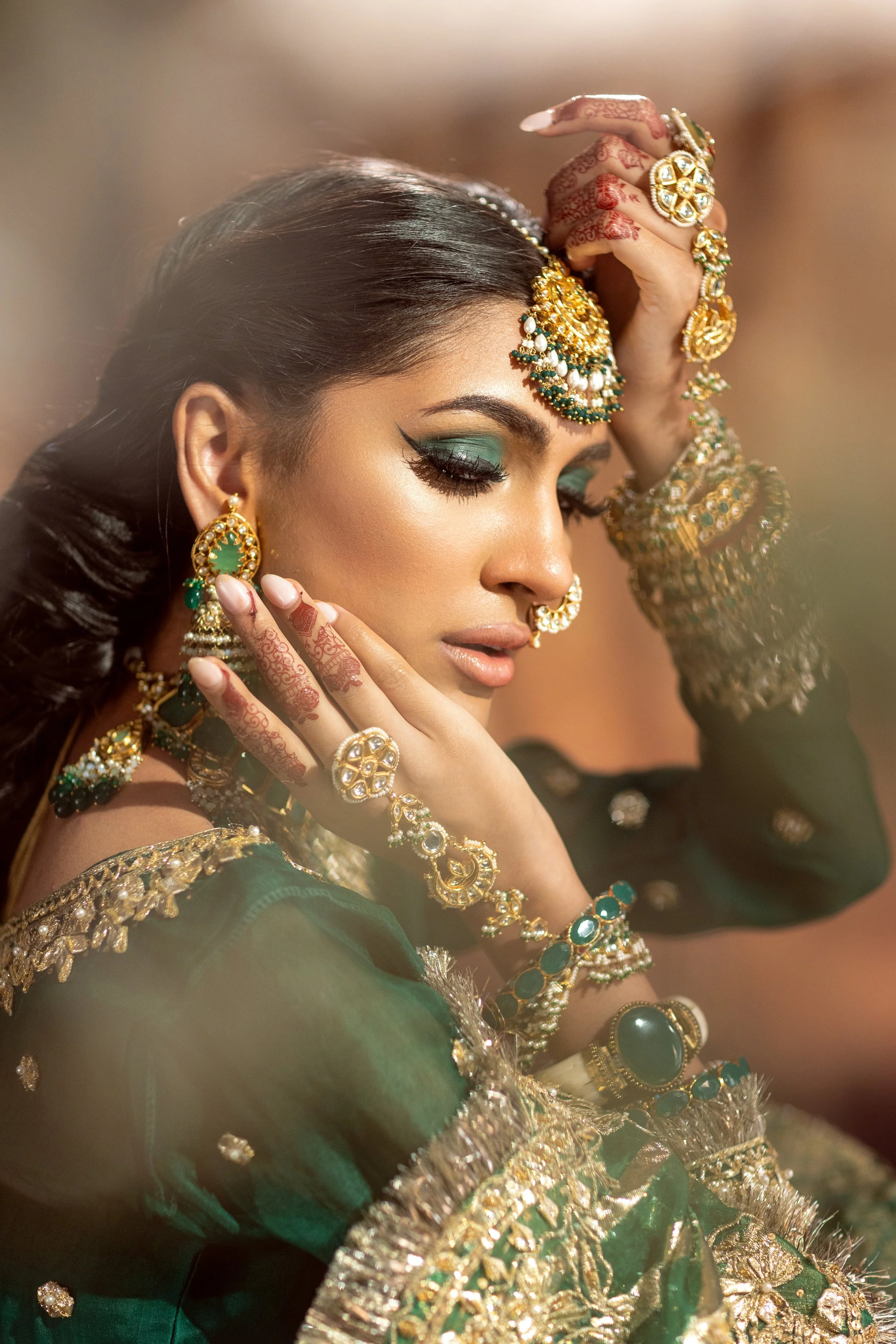 A woman dressed in traditional Indian attire with elaborate gold jewelry and henna on her hands, gracefully posed with her eyes closed.
