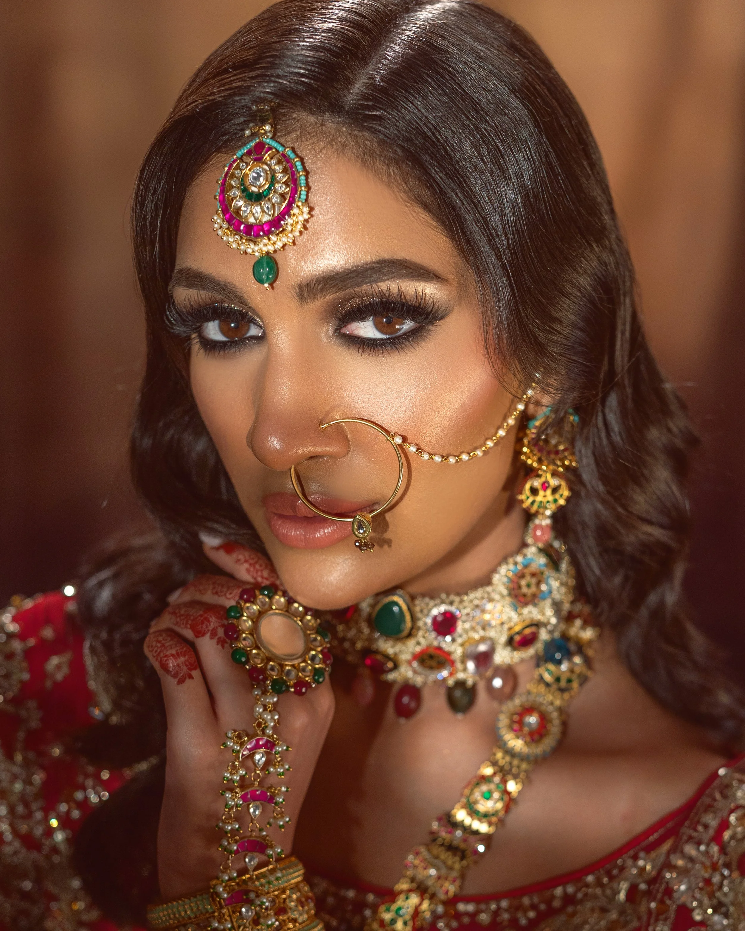Close-up of a woman wearing traditional Indian jewelry, including a headpiece, nose ring, earrings, and multiple necklaces, with intricate jewelry designs and a red outfit.