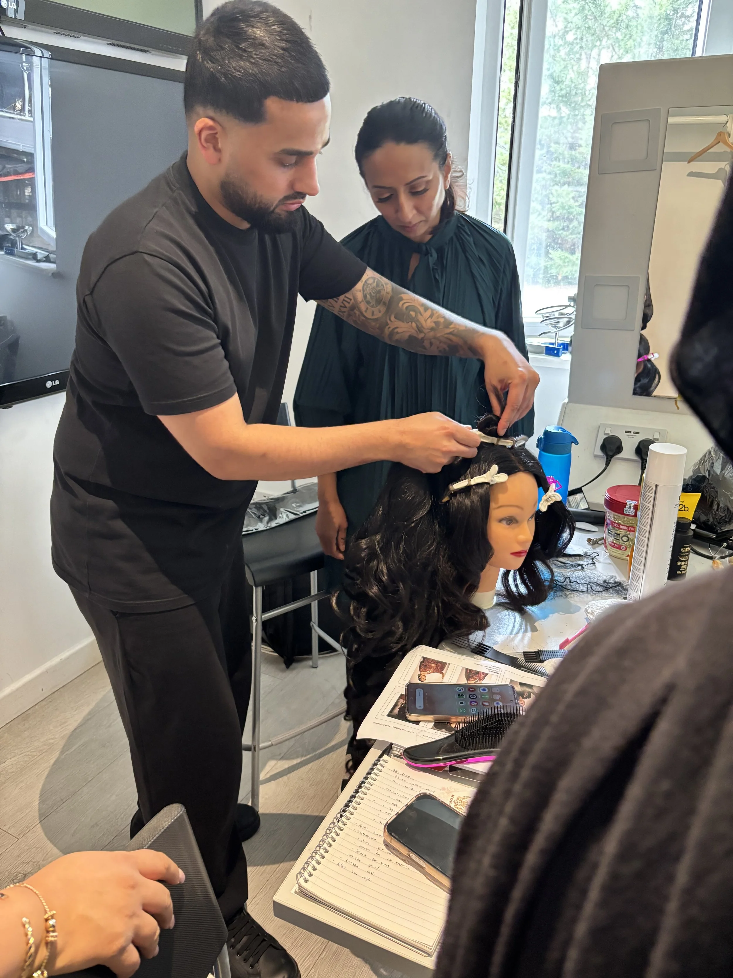 A hairstylist working on a woman's hair in a salon, with various hair styling tools and products on the table.