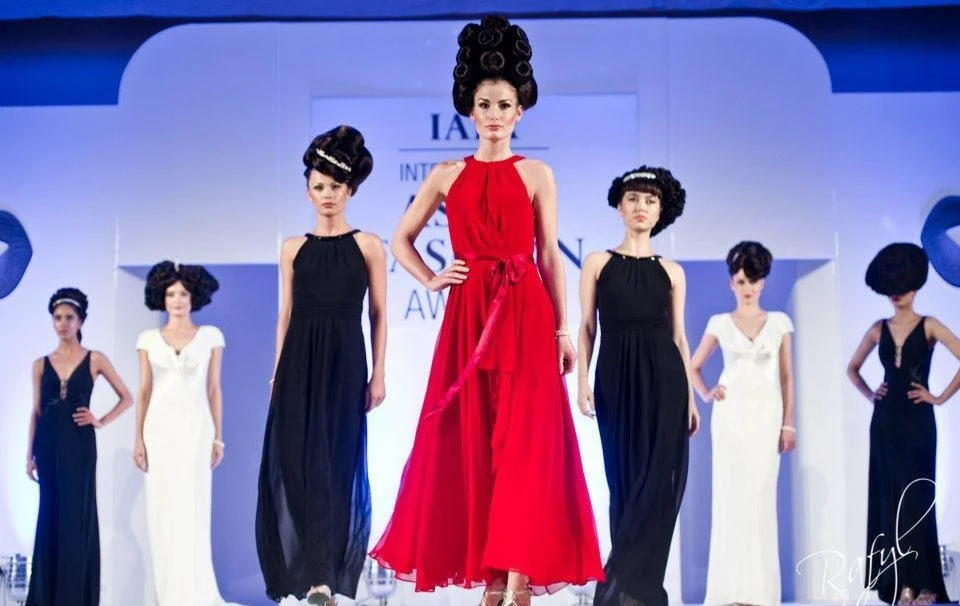 Models walking on runway at a fashion show, wearing long dresses in black and white, with elaborate hairstyles, and posing confidently.