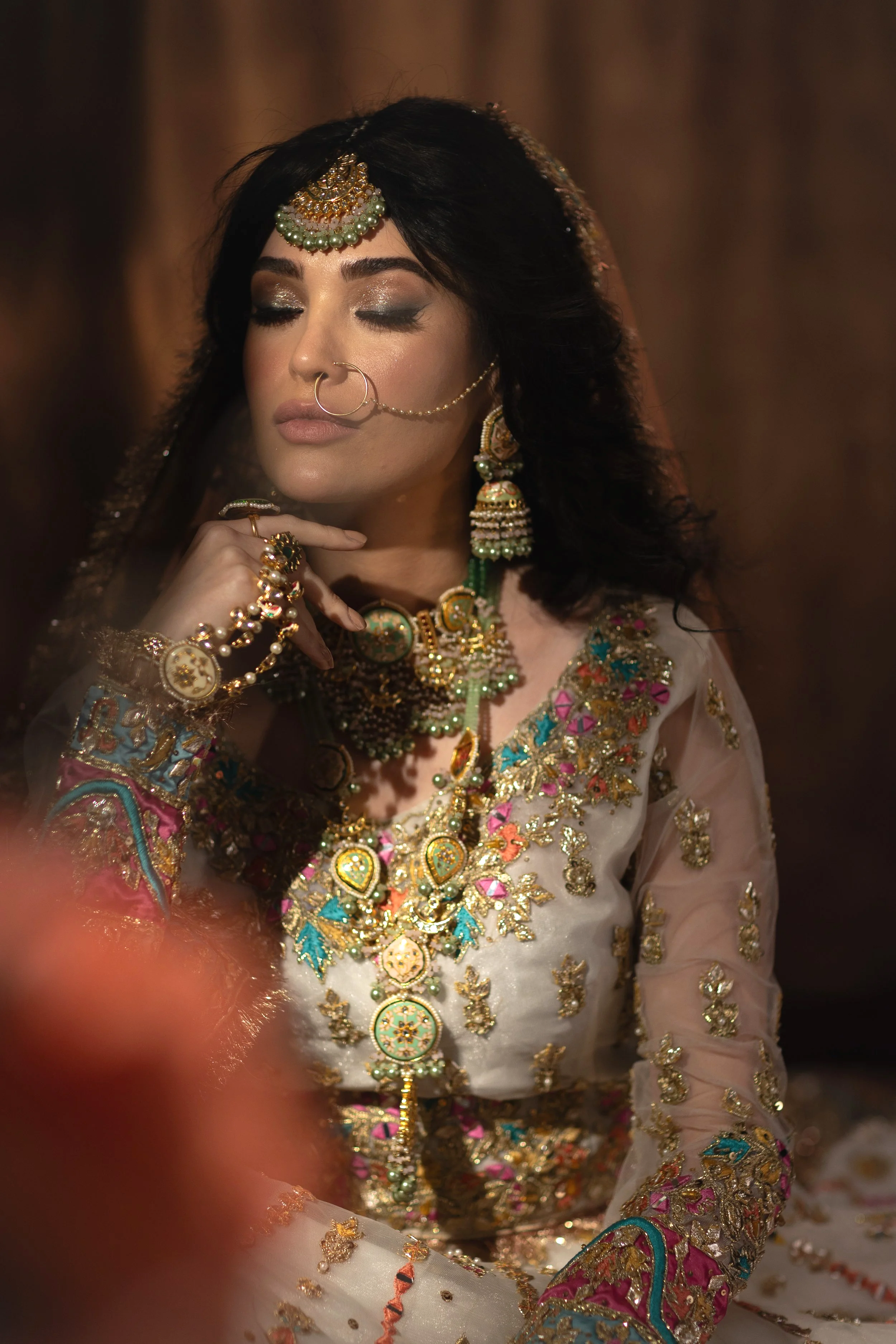 Woman wearing traditional Indian attire and jewelry, with her eyes closed, in a contemplative pose.