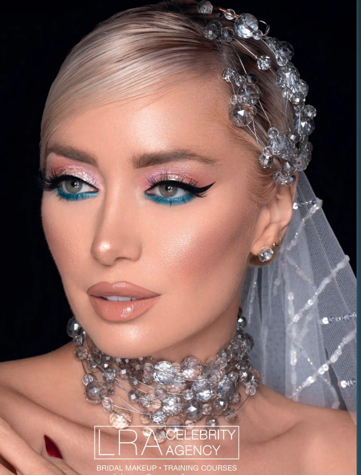 Close-up of a woman with bridal makeup, wearing multiple crystal jewelry pieces including earrings, necklace, and headpiece, with a veil in the background.