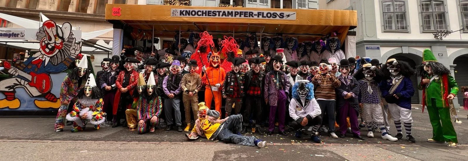 Gruppe von Menschen in bunten Clown- und Maskenkostümen bei einem Karnevals- oder Fasnachtsumzug auf der Straße.