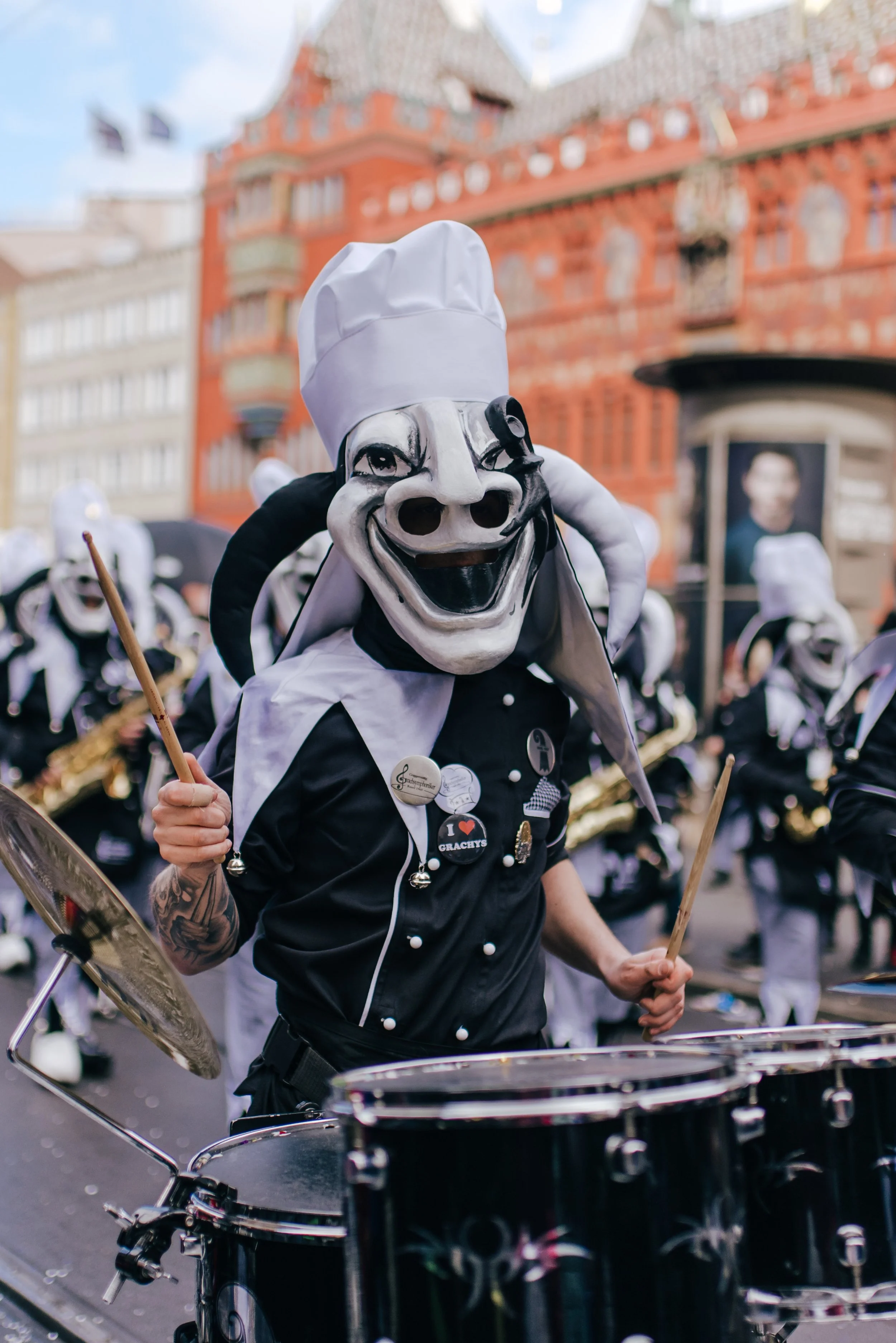 Mann in einer Band mit einem riesigen Gummihorn-Maskenball, der als Koch getragen wird, spielt die Trommel während eines Marsches auf einer Stadtstraße.