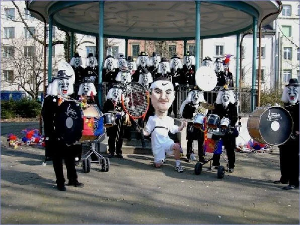 Eine Gruppe von Menschen in Karnevalskostümen mit großen Masken und Musikinstrumenten auf einem Karussell im Freien.